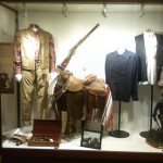 Three main items left to right are a costume from Big Jake, saddle from The Cowboys, and shirt from The Man Who Shot Liberty Valance.