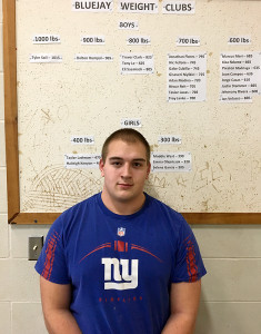 Perry junior Tyler Soll is currently the lone member of the 1,000-pound club at PHS. He stands near the results of the Feb. 25 Lift-a-Thon. Photo by Scott Pierce.