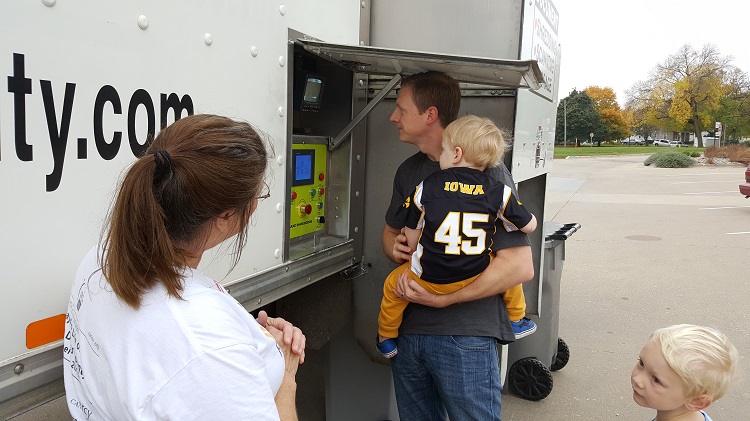 Perry Public Library Director Mary Murphy invited Perry Hy-Vee Store Director Matt May and his young sons, Wilson, in arms, and Lincoln, to inspect the recycling machinery at the library's annual free shredding event Saturday.