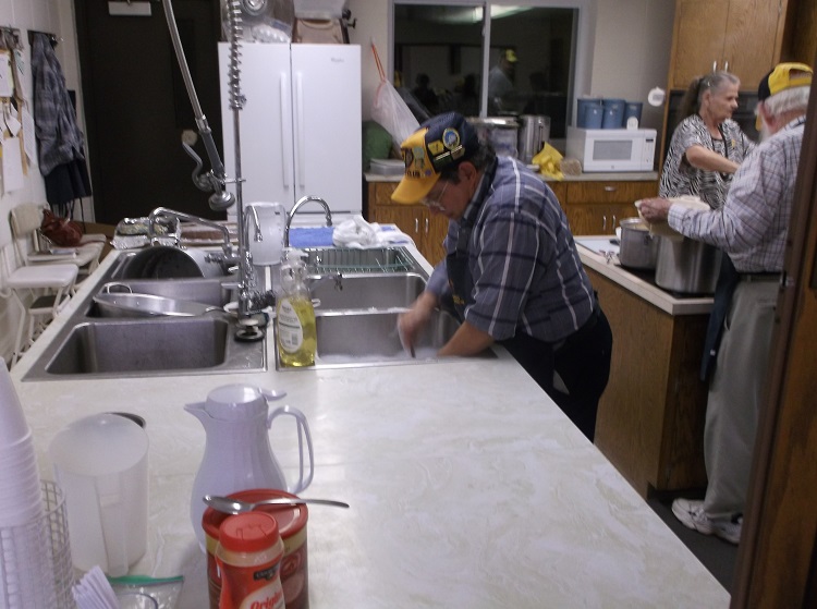Never one to shy away from pitching in, Rick Liebich, left, washes the many dishes created at the Rippey Lions Lions spaghetti dinner. On the right, Mary Liebich and Phil Roberts prepare for more diners.